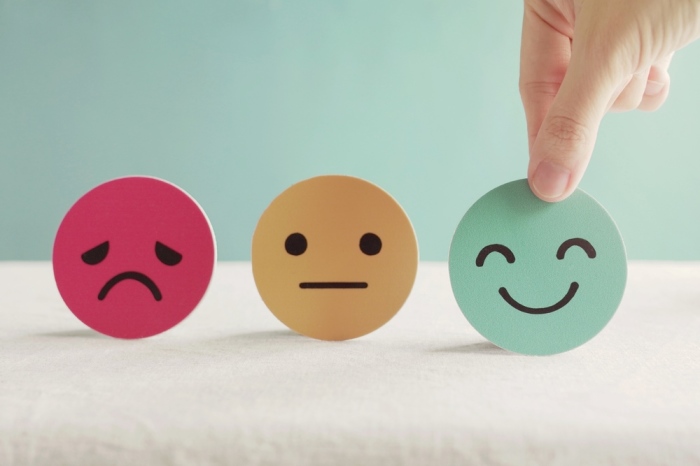 Hand selecting a smiley face card from three emotion cards (sad, neutral, happy) representing varied emotional responses.