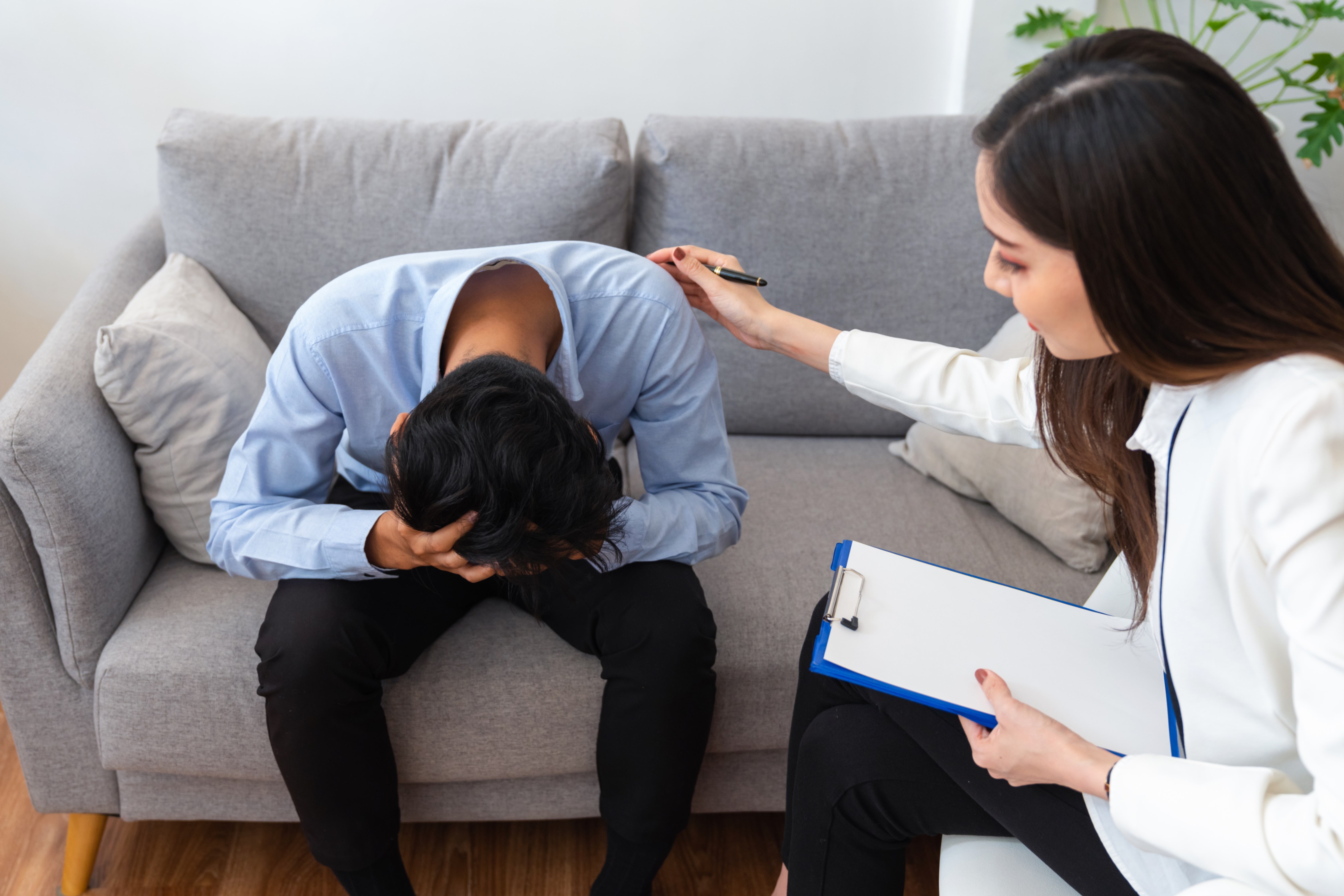 A female therapist offering support to a distressed young man during a counselling session.