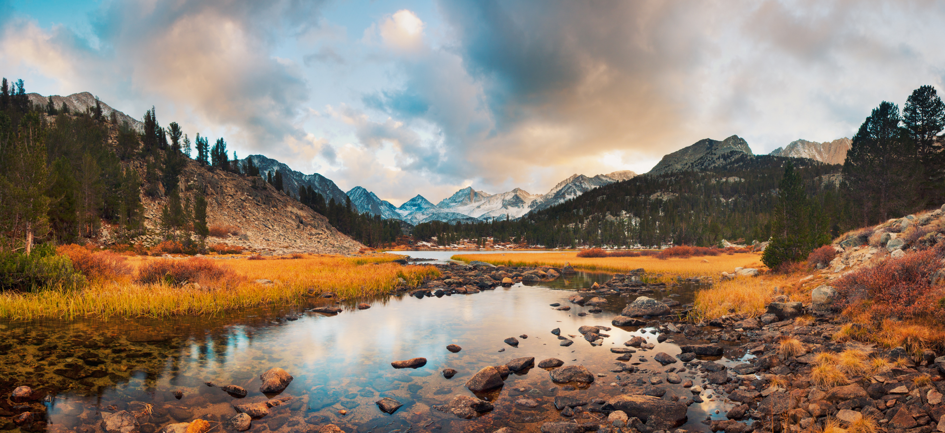 Scenic view of a mountain lake surrounded by autumn foliage and rocky terrain under a cloudy sky.