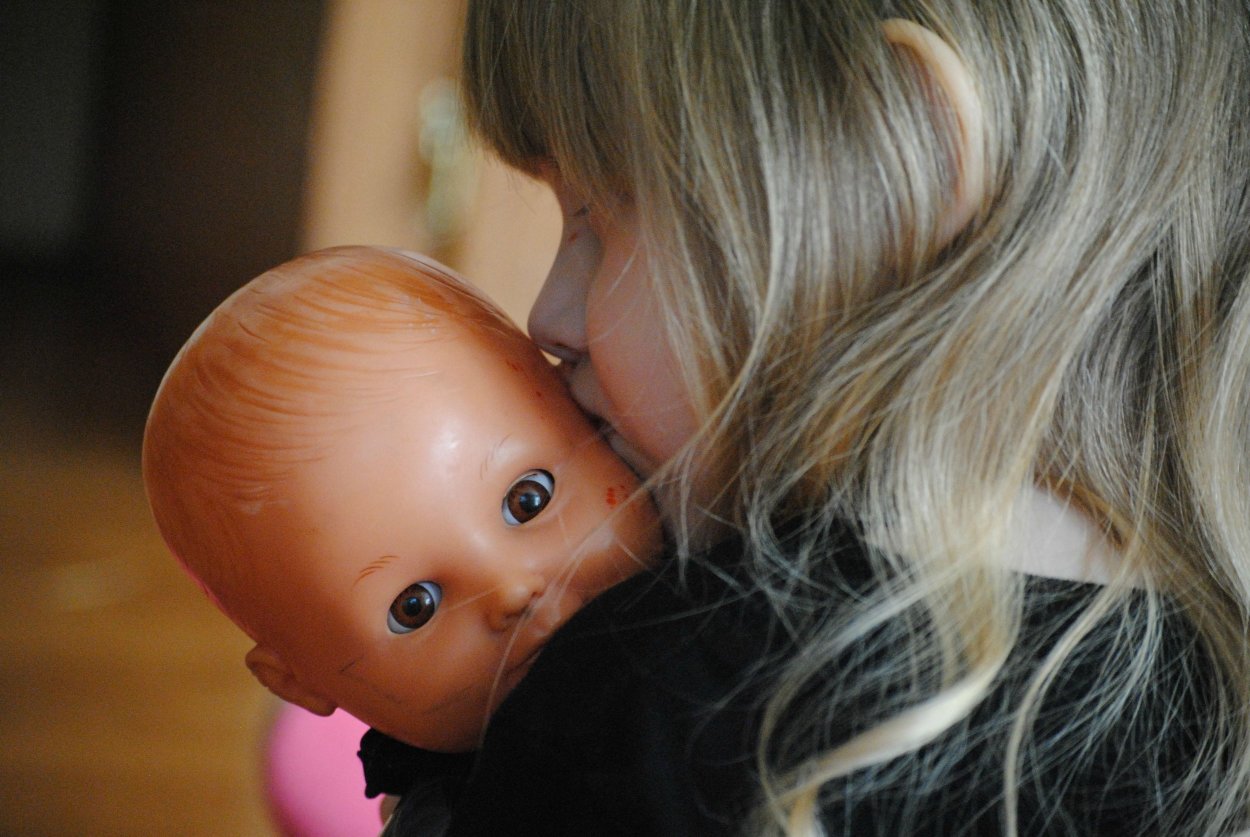 Exploring feelings of comfort and connection, this child shares a tender moment with a doll, reflecting the importance of emotional support in mental health.