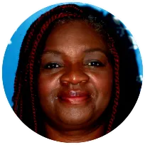 Alt text: Integrative counsellor with braided hair smiling warmly against a blue background, reflecting a welcoming presence.