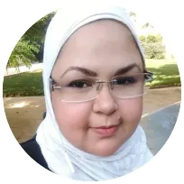 Professional psychotherapist wearing a white hijab and glasses, smiling outdoors, representing expertise in mental health services.