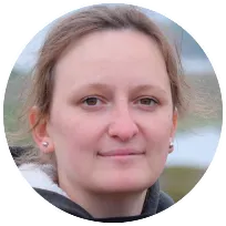 A woman with short hair and a thoughtful expression stands outdoors, representing a psychotherapist's compassionate approach.