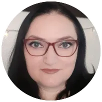 Woman with long black hair and glasses, smiling confidently, offering counselling, therapy, and wellness services for adults.