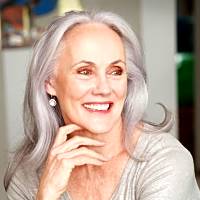 Smiling older woman with long gray hair and earrings, embodying the joy of nostalgic memories related to Proust's themes.