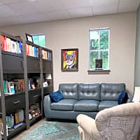 Helping improve couple's relationships & individual's well-being through integrative psychotherapy -Tampa & Safety Harbor FL (also online) Cozy therapy room featuring a blue couch, a bookshelf filled with books, and calming artwork on the walls.