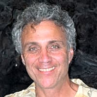 Smiling man with curly hair, reflecting themes of mentalization and mindfulness in a serene setting.