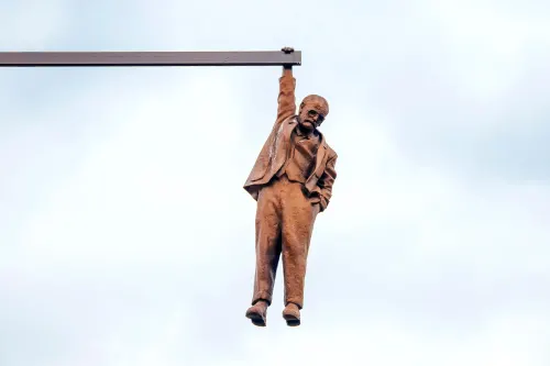 Bronze sculpture of a man in a suit hanging from a beam, representing themes of struggle and resilience in psychoanalysis.