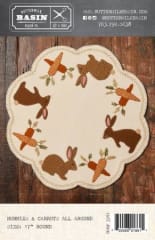 BUNNIES & CARROTS WOOL MAT PATTERN from Buttermilk Basin shows a cream colored mat with brown bunnies and orange carrots all around.
