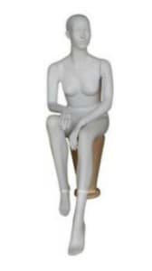 Matte white fiberglass sitting female mannequin with a smooth egghead, posed elegantly with hands in her lap, ready for clothing display in a retail setting.