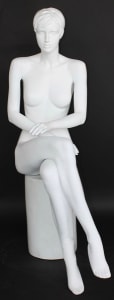 Matte white fiberglass female seated mannequin with molded hair and crossed legs, showcasing fine facial details for retail display.