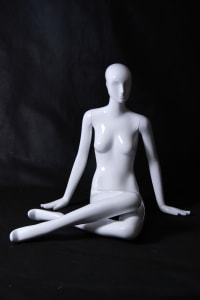 Seated female abstract mannequin in a glossy white fiberglass finish posed on the floor for retail display.