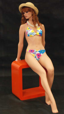 Elegant sitting female mannequin in a realistic fleshtone finish on a round metal base, made of durable fiberglass for high-end boutique displays.