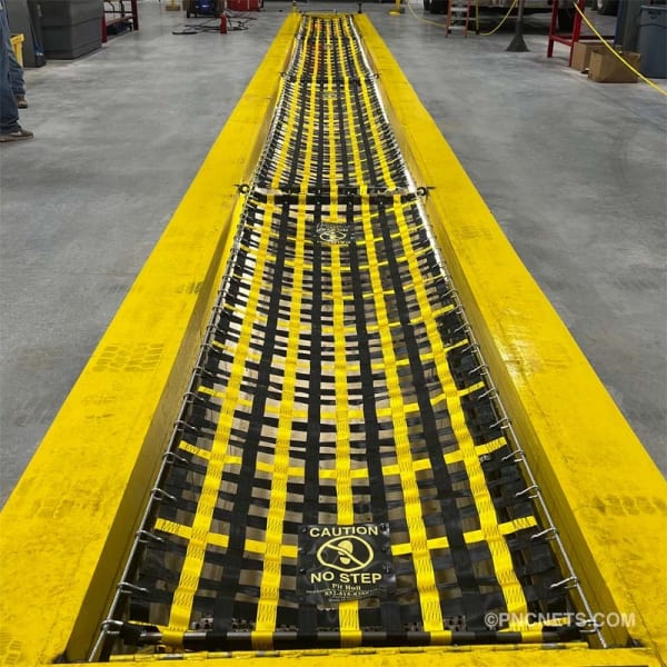 Yellow and black pit cover safety net with 'Caution No Step' warning at an automotive quick lube bay, ensuring safety around the service pit.