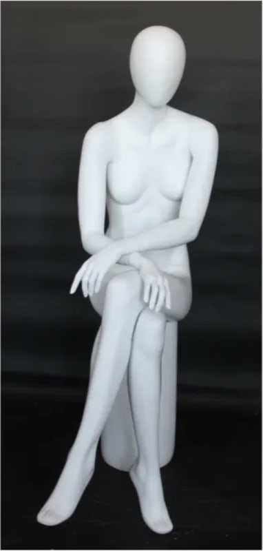 Female egghead mannequin in seated pose. Her legs are crossed with her hands on her lap.