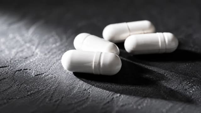 Gélules blanches en gros plan sur une ardoise sombre
