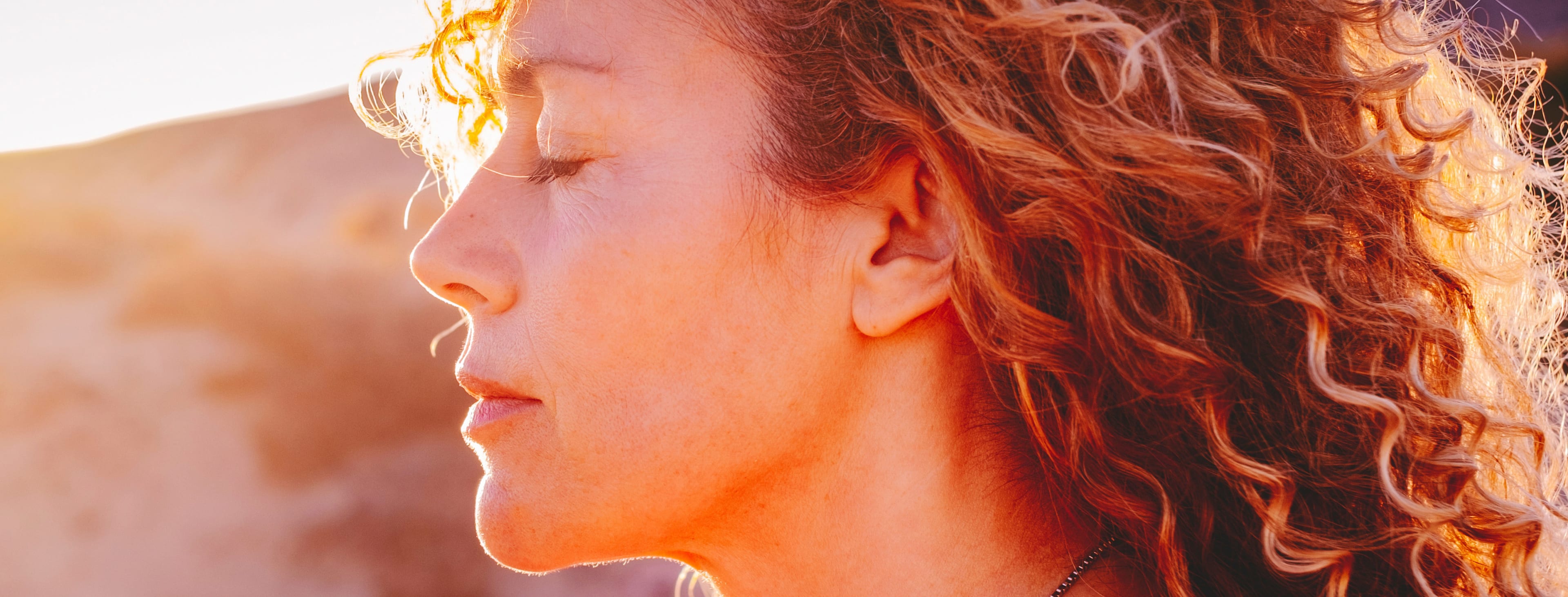 Close up sunset portrait of attractive woman with closed eyes and sun in back light. 