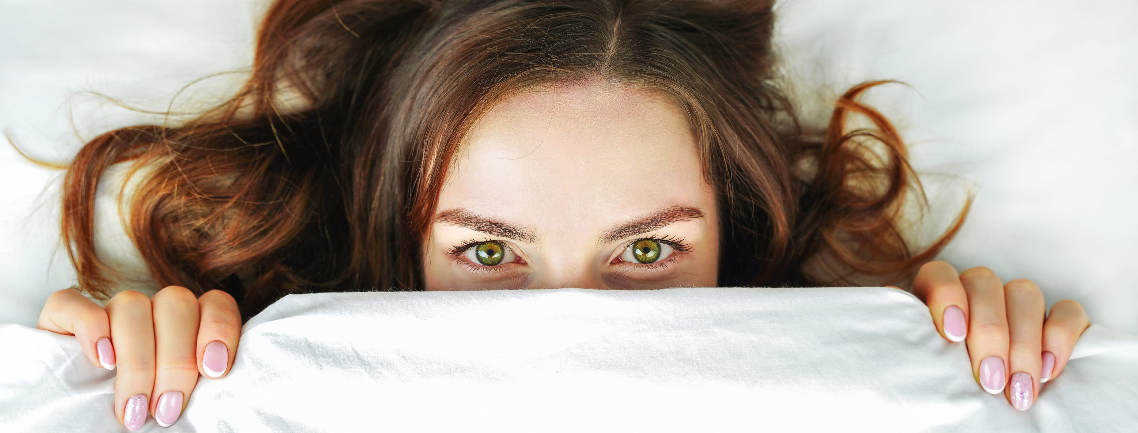 Closeup of woman in bed peeking out over covers that are pulled up to her eyes
