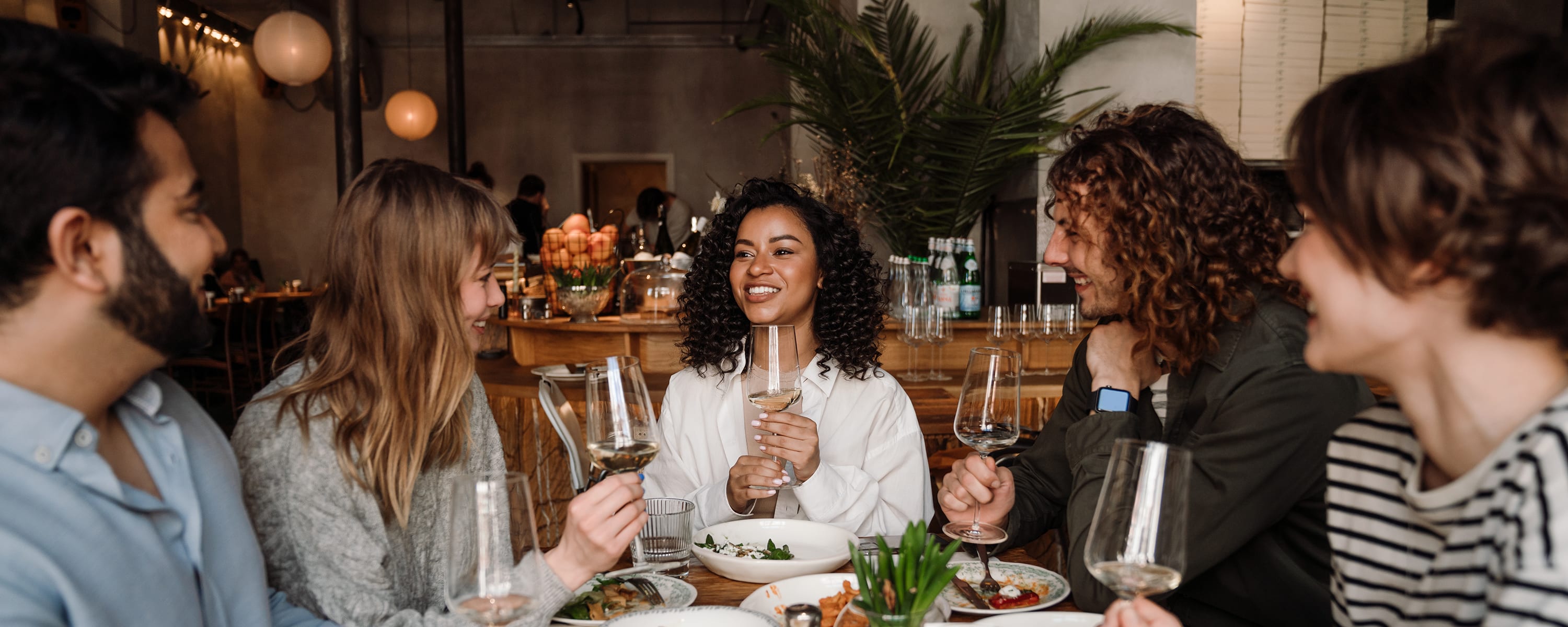Group of cheerful friends talking and drinking wine while dining in restaurant