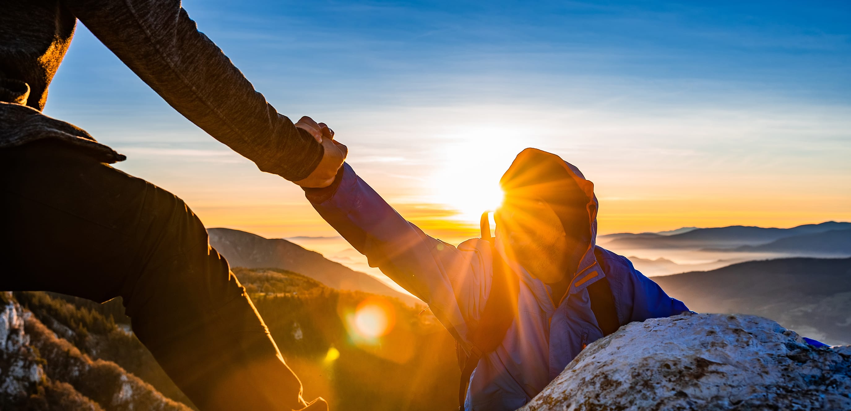 Man reaching helping had to another man with mountains and sunrise in background