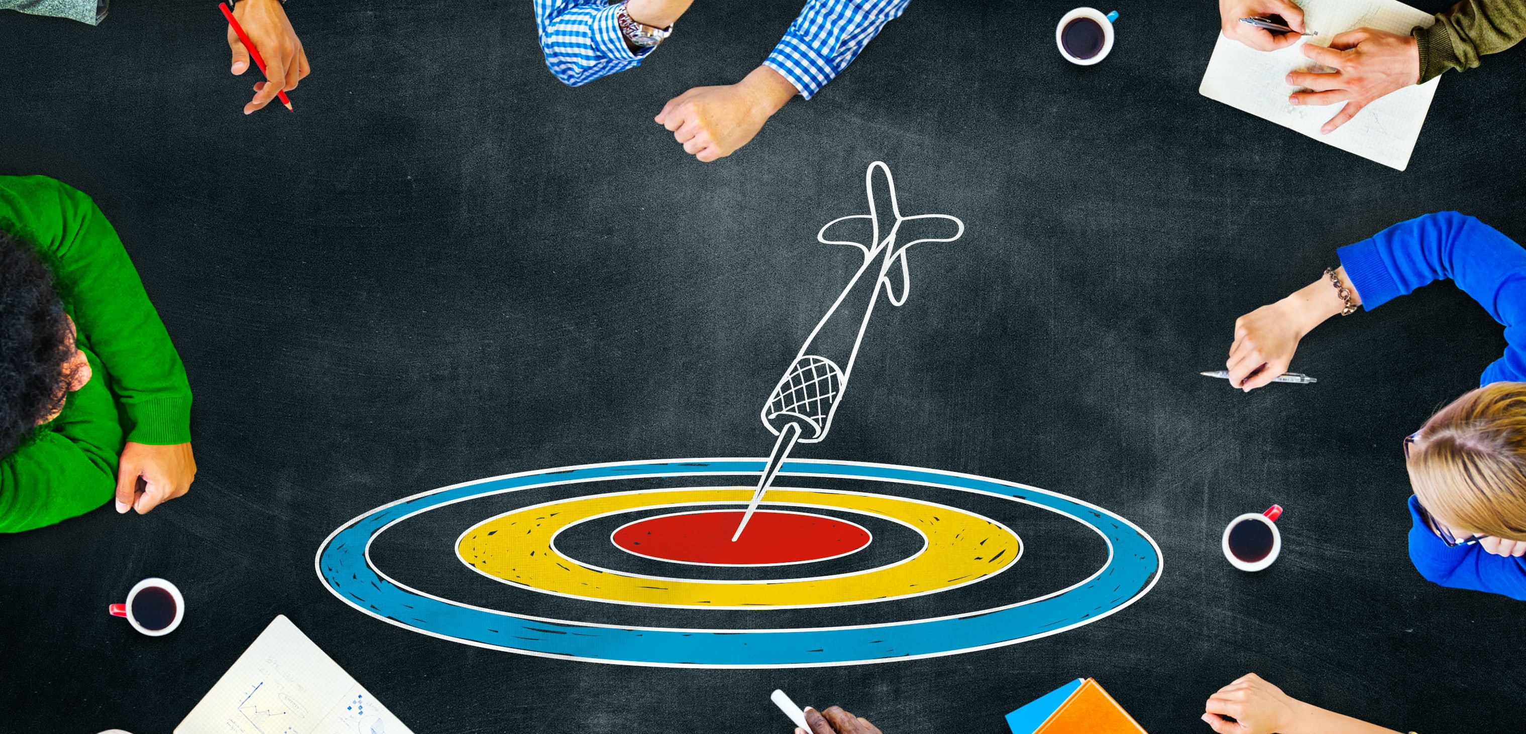 A team sitting around a chalk drawing of an arrow stuck in a bullseye