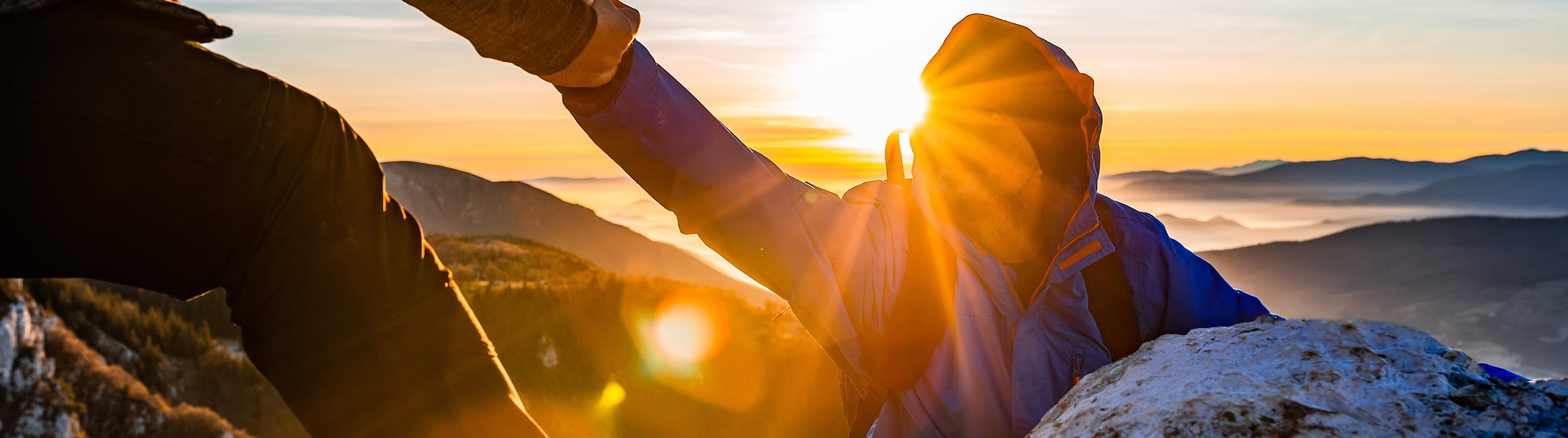Man reaching helping had to another man with mountains and sunrise in background