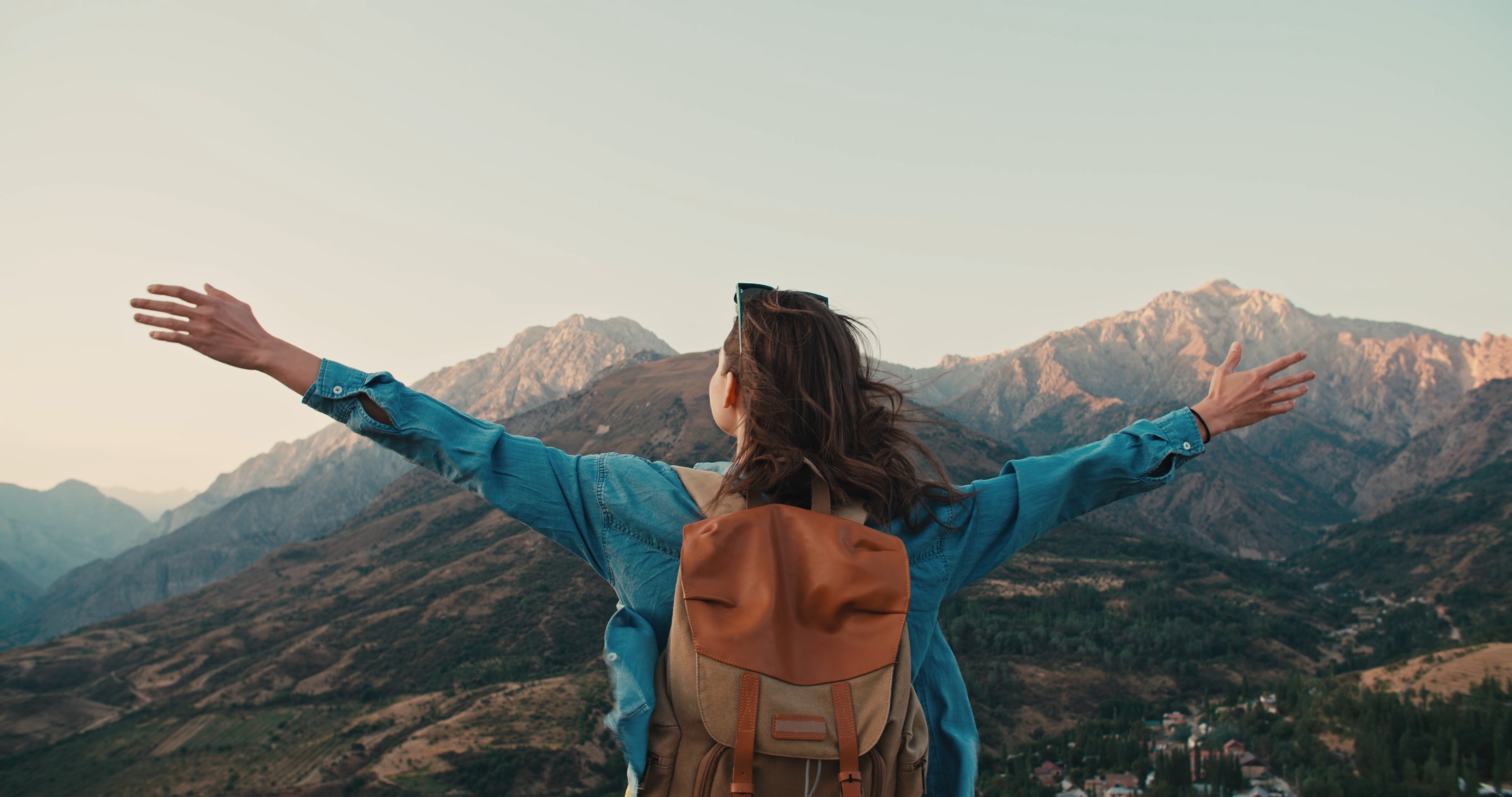 Woman facing away raising arms toward mountains {3000x2000}