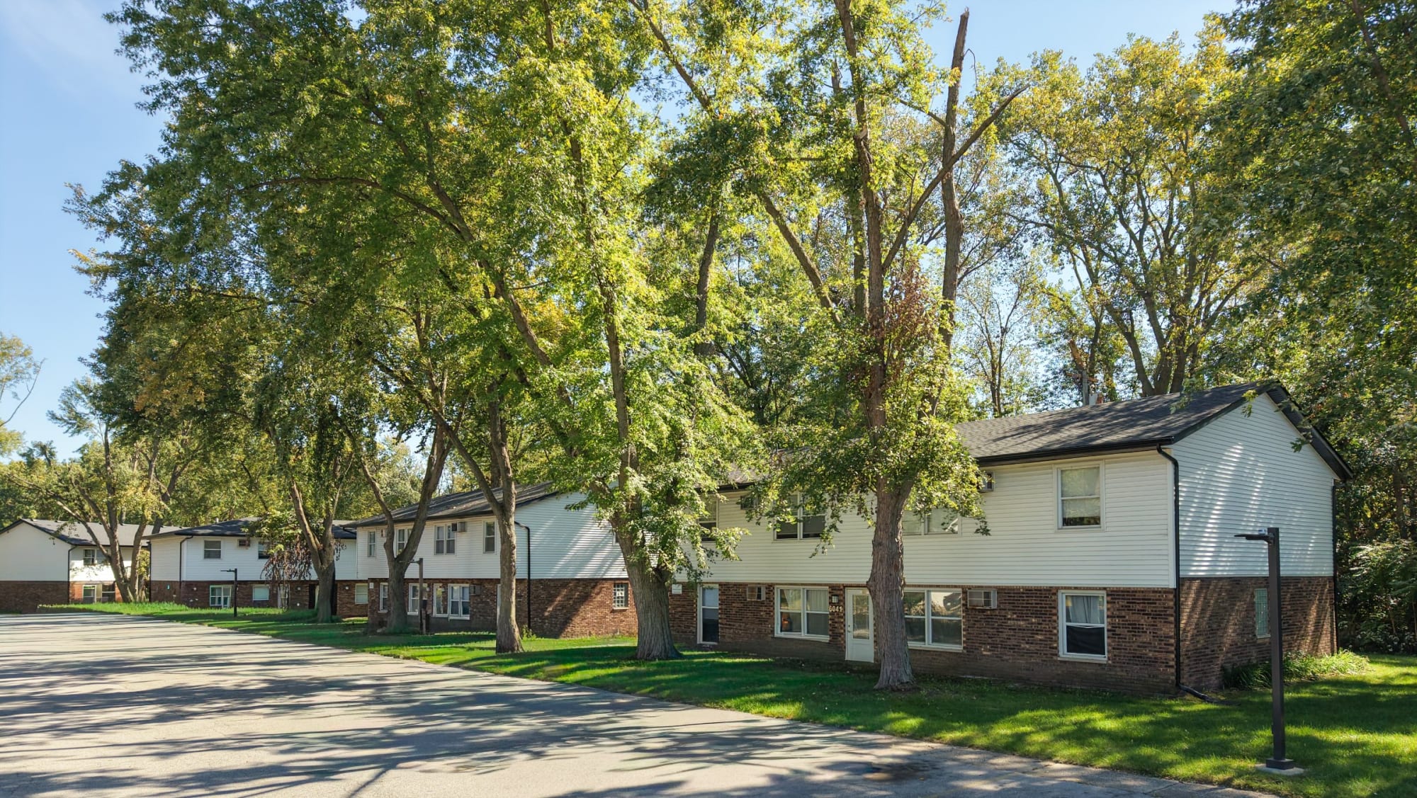 Two-story brick and siding buildings beneath mature trees along the drive