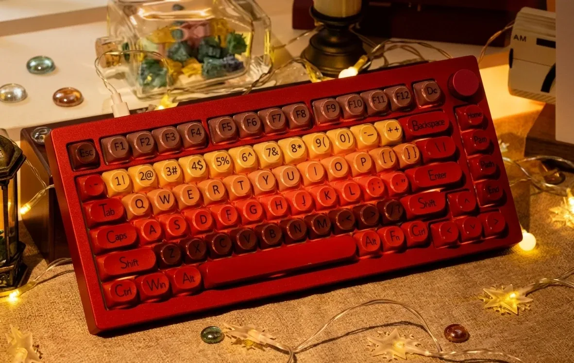 Primo piano di una tastiera meccanica rossa AKKO 5075 X Veekos K75 con copritasti a profilo tondo con sfumature dal giallo al marrone, manopola rotante e luci calde d&rsquo;atmosfera sullo sfondo.