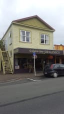 Golden Bay Organics shopfront in Takaka, New Zealand, showcasing organic food and products in a light green building with a dark brown awning and external stairs.