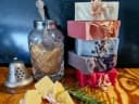 Colourful stacked artisan tallow soap bars with botanicals, displayed with raw ingredients and rosemary for Fatglow Tallow Soaps.