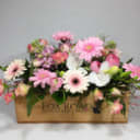 Vibrant pink and white florist arrangement in a rustic wooden planter box, featuring gerberas, hydrangeas, and roses.