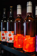 Bottles of Known Unknown Wine, featuring vibrant orange and red labels, displayed on a shelf. Artisan wine from Taranaki.