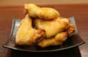Pile of golden-brown glazed chicken wings on a dark square plate, a delicious prepared food item from Lucky Pig.