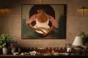 A bountiful table of prepared foods: artisan pizzas, fresh salads, and desserts, in a warm dining setting with a chef painting. Represents Mamas' offerings.