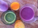 Colourful fresh juices and smoothies in glasses and bottles on a rustic wooden table, showcasing Ronia and Pippi's beverages at an NZ farmers market.