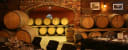 Rustic wine cellar with stacked wooden barrels and tables set for tasting, featuring menus from Vegoud Winery.