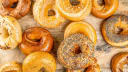 Assortment of freshly baked artisan bagels, including sesame, poppy seed, and onion, on a rustic wooden surface by Holy Bagal.