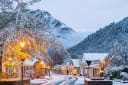 Snowy street scene in a historic New Zealand town near Queenstown, with glowing streetlights, old buildings, and snow-capped mountains.