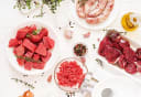 Fresh raw beef cuts, ground mince, and sausages with thyme, garlic, and spices, prepared by a New Zealand butcher.