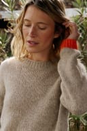 Woman with blonde hair in a beige knitted sweater with bright orange cuff, looking down. No craft or market context for Shopology visible.