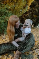 Mother and baby in green velvet, surrounded by autumn leaves. SimplyStone crafts maker Sara and child at Queenstown market.