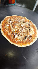 Uncooked artisan pizza topped with sliced mushrooms, black olives, cheese, and black sesame seeds on a dark surface, representing Abdal's Gourmet Foods at Otago Farmers Market.