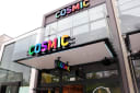Modern building exterior with colourful 'COSMIC' signs on two levels and a hanging sign, glass facade.