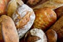 Assortment of freshly baked artisan bread loaves, including rustic, flour-dusted, and focaccia styles, from a baker.