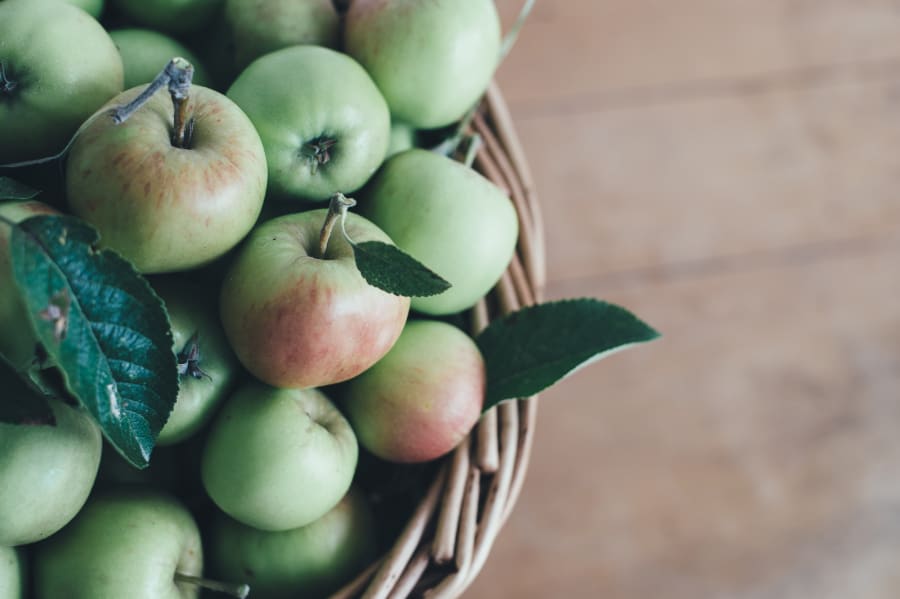 Freshly picked green and red apples with leaves in a woven basket, ready for sale at Peelview Orchard.