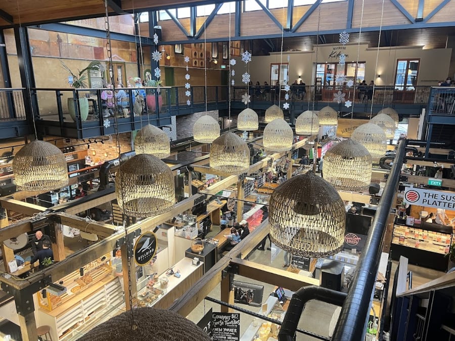 Bustling multi-level indoor market with various food and craft stalls, diners, and unique wicker light fixtures.