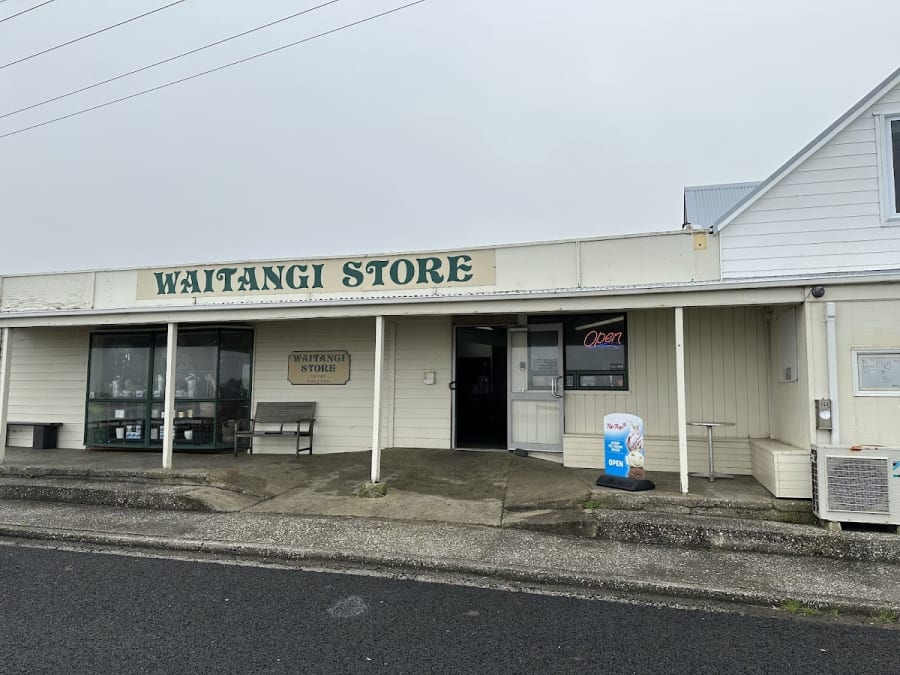 Exterior of Waitangi Store, a small town general store with a porch and window displays, featuring an 'Open' sign and a Tip Top ice cream sign.