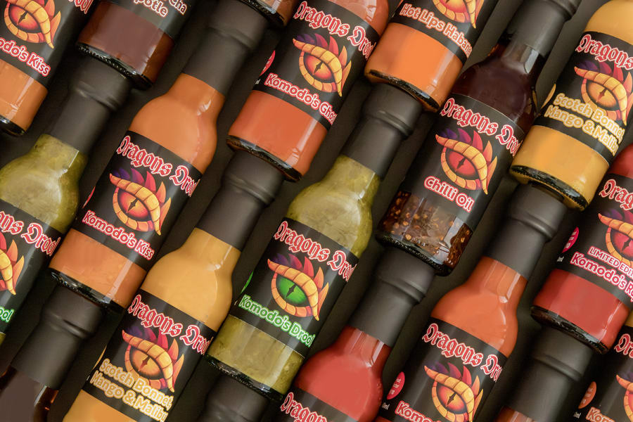 A vibrant array of Dragon Drool Hot Sauce bottles, featuring flavours like Komodo's Kiss and Chilli Oil, artisan condiments.