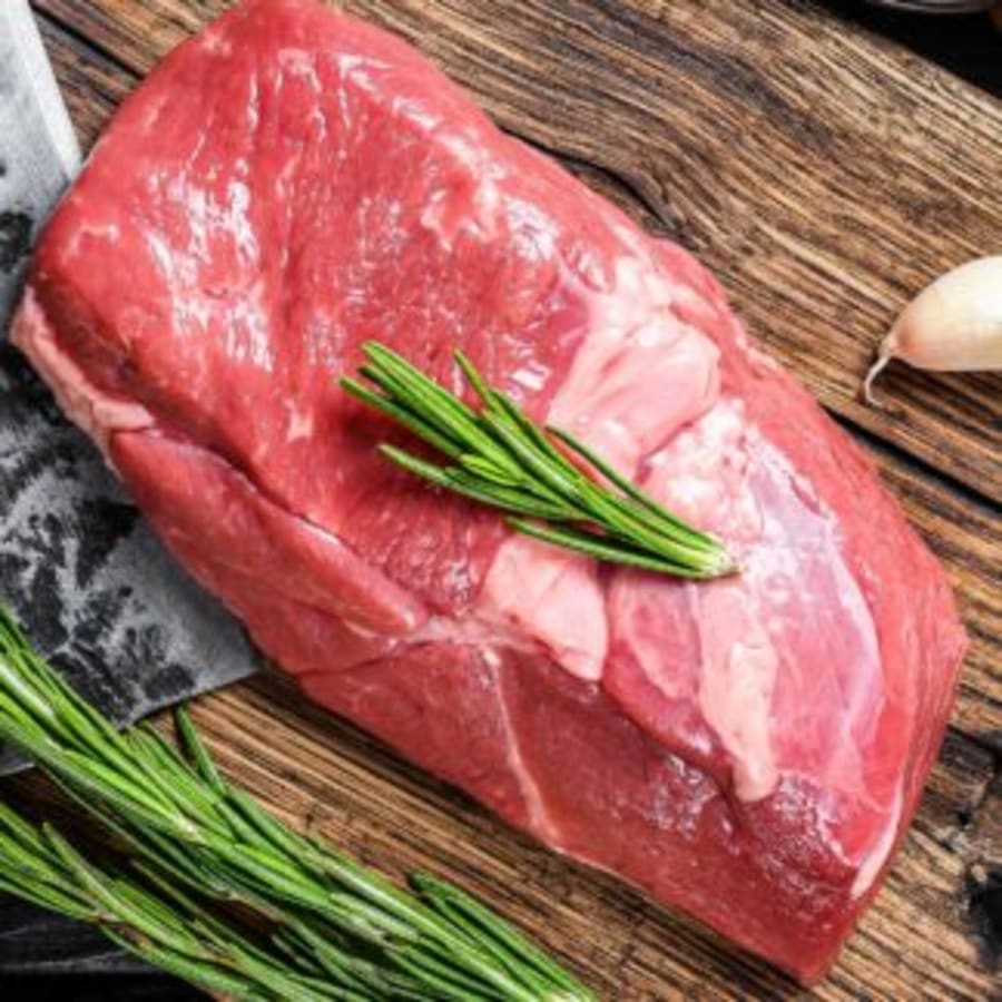Fresh raw beef roast with sprigs of rosemary and garlic on a rustic wooden board, representing Ellis Creek Farm, a Nelson butcher.